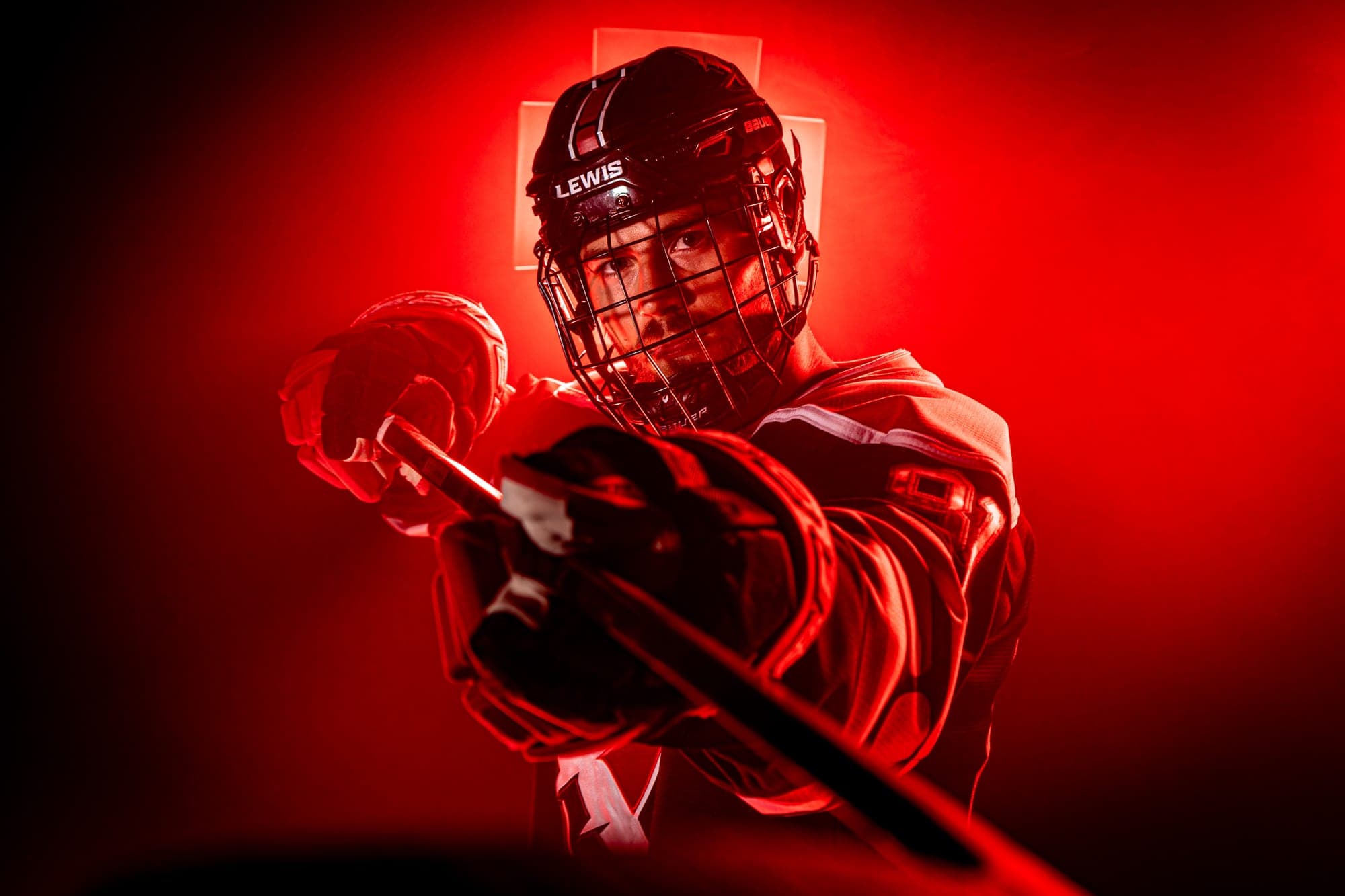Lewis hockey player lit in red, mid-swing with his stick, in a dramatic media day portrait