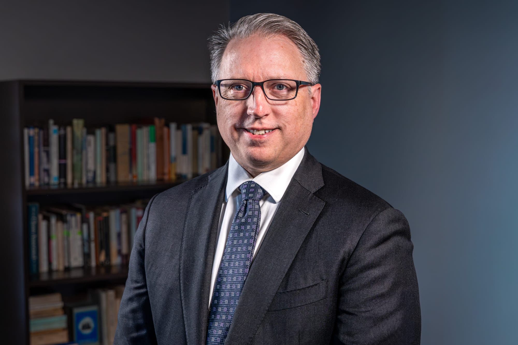 Executive headshot of a man in a suit in front of a bookshelf
