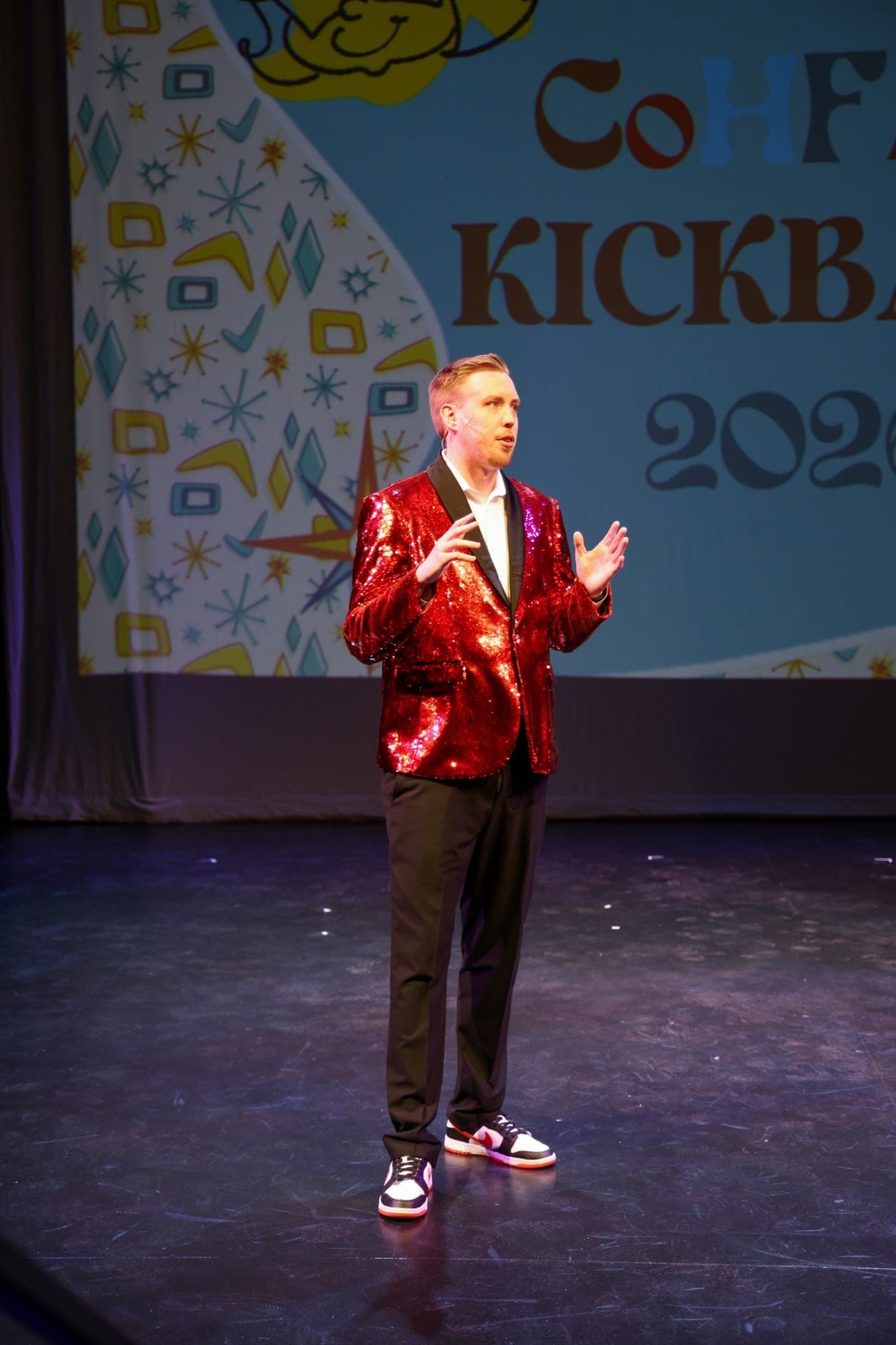 Logan Kap in a red sequin jacket hosting the CoHFAC Kickback on stage at Lewis University