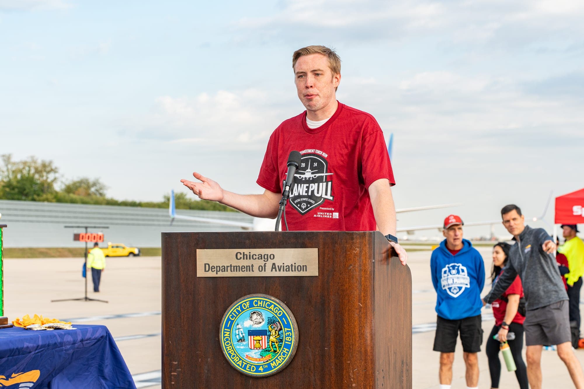 Logan Kap emceeing the Special Olympics Illinois Plane Pull from the podium at O'Hare